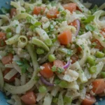 A bowl of vibrant cebolla ensalada, featuring thinly sliced onions, peas, diced carrots, and fresh herbs.