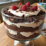 A decadent chocolate trifle in a glass trifle dish, layered with rich chocolate cake, creamy whipped topping, and garnished with fresh raspberries and chocolate crumbles.