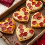 Heart-shaped mini pizzas on a wooden tray with Valentine’s decorations.