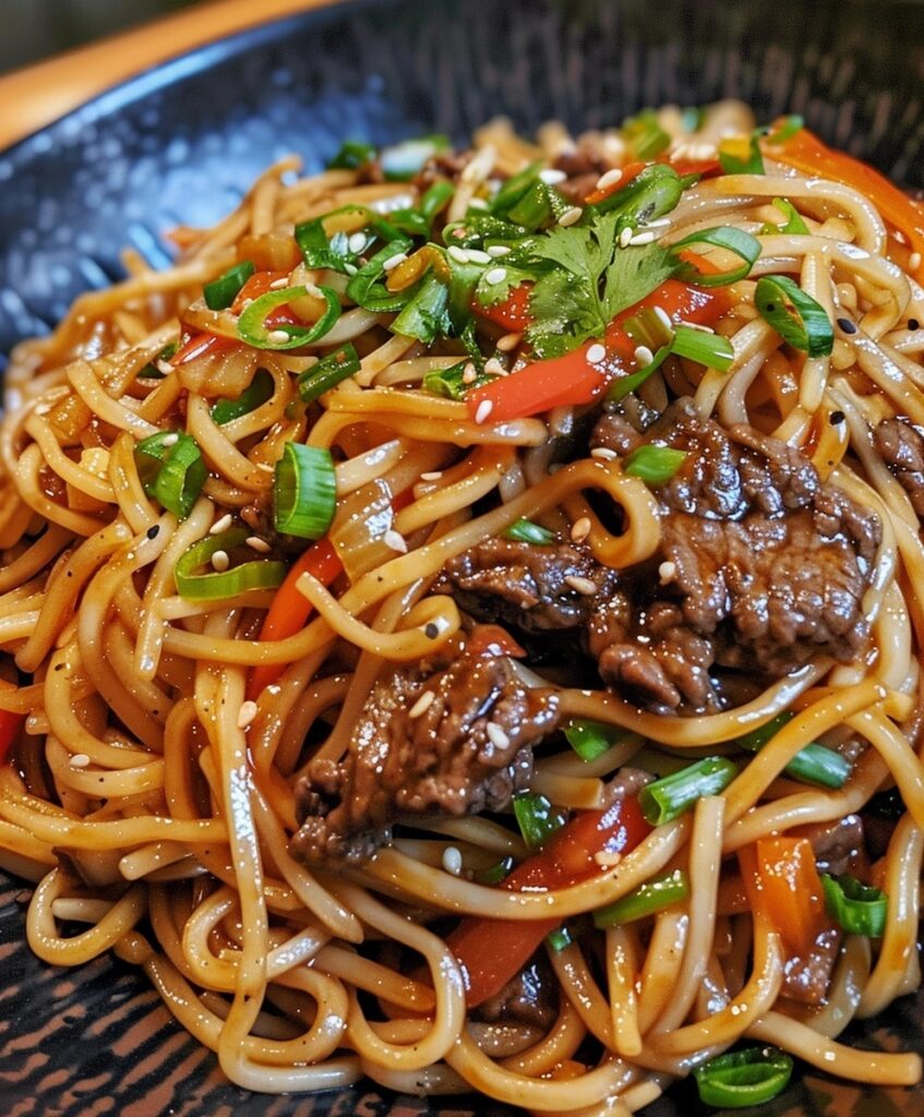 A close-up of Sticky Beef Noodles in a dark bowl, showing thin noodles, tender beef, colorful vegetables, sesame seeds, and green onions.


