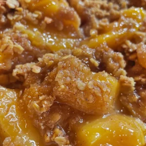 Bowl of peach crisp topped with a scoop of vanilla ice cream.