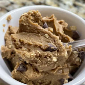 Delicious protein cookie dough in a small white cup, surrounded by chocolate chips.