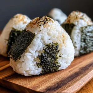 Several onigiri, Japanese rice balls, topped with sesame seeds and seaweed, arranged on a white plate.